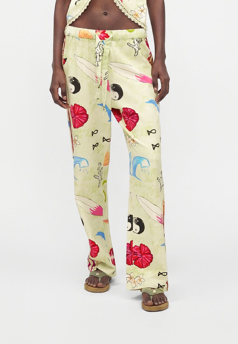 Γυναίκα που φορά φαρδιά ανοιχτό κίτρινα παντελόνια με πολύχρωμα θαλάσσια και λουλουδάτα σχέδια, όρθια ξυπόλητη με τα πόδια ελαφρώς ανοιχτά.