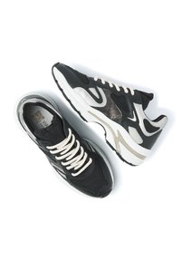 Black athletic sneakers featuring a mesh upper, beige accents, a cushioned sole, and white laces. Textured plastic detailing along the sides.