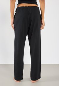 Pantalons noirs, légers, à jambes larges avec une taille élastique, affichant une texture lisse et une coupe ample, adaptés pour un usage décontracté.