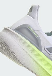 Jasnoszare buty do biegania z teksturowanym cholewką z dzianiny i szarymi akcentami. Posiadają logo "ULTRABOOST" oraz podeszwę z zielonymi akcentami.