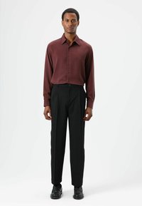 Chemise à manches longues couleur bordeaux avec fermeture par boutons, associée à un pantalon noir ajusté. Tissu lisse avec une coupe classique. Chaussures de ville noires.