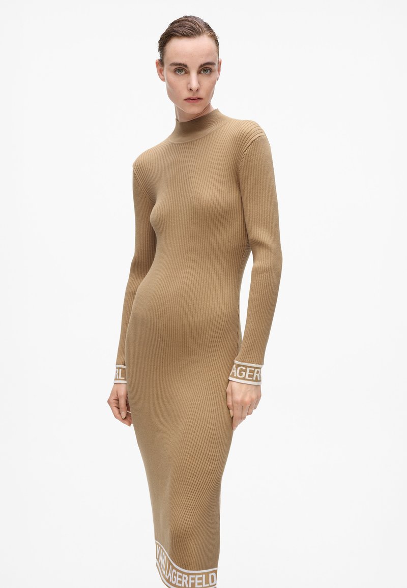 Abito a maglia a maniche lunghe a coste in beige con colletto alto. Presenta il logo in contrasto "LAGERFELD" su polsini e orlo. Silhouette aderente.