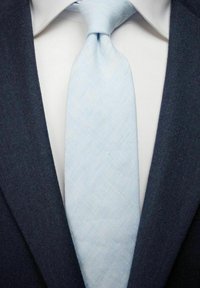 Vaaleansininen teksturoidu solmio tummansinisen puku takin ja valkoisen paidan alla, korostaen siistejä linjoja ja muodollista ilmettä.