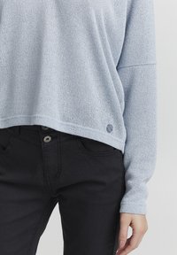 Maglione azzurro chiaro a maglia con una vestibilità morbida e una trama sottile, abbinato a jeans neri con bottone e tessuto liscio.