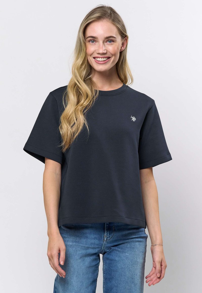 T-shirt oversize gris foncé en coton doux, avec manches courtes et col rond, arborant un petit logo sur la poitrine.