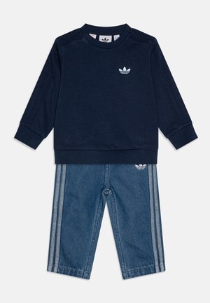 Marineblauer Sweatshirt mit weißem Logo, langen Ärmeln und gerippten Bündchen, kombiniert mit blauen Denim-Hosen mit weißen Seitenstreifen und Logo.