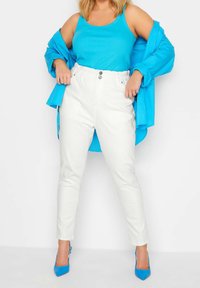 White high-waisted pants with elastic waistband and front buttons, paired with a blue tank top and matching button-up shirt. Blue heels.