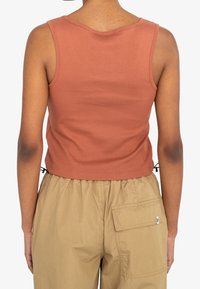 Débardeur côtelé couleur rouille avec un design ajusté et un col rond. Comprend une longueur raccourcie et des liens latéraux réglables.