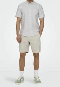 Lyhythihainen, kauluksellinen paita vaaleansinisellä sävyllä, ohuilla valkoisilla raidoilla, yhdistettynä teksturoituihin vaaleisiin shortseihin ja mintunvihreisiin tennareihin.