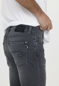 Graue Denim-Jeans mit schmaler Passform, ausgestattet mit einem schwarzen Lederpatch am hinteren Bund und kontrastierender Naht an den Taschen.
