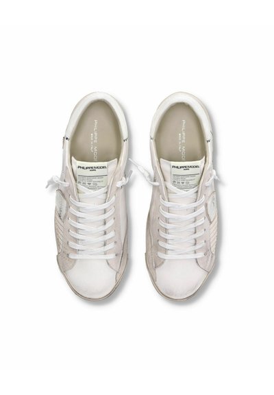 Sneakers bianchi con tomaia in pelle leggermente testurizzata, lacci piatti e un logo discreto sulla linguetta e sui lati. Punta arrotondata e design semplice.