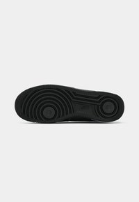 Black rubber sole with circular pattern and textured edges, featuring two circular indentations and raised branding detail.