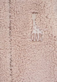 Tessuto fuzzy di colore rosa pallido con una finitura strutturata. Presenta una toppa ritagliata con ricami beige che assomigliano a un disegno di giraffa.