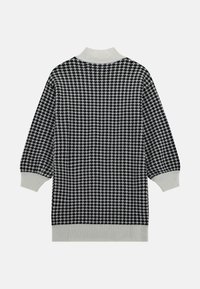 Juodai baltas šunų dantų rašto megztinis su aukštu įribotu apykakle ir įribotais rankogaliais. Tekstūruota medžiaga, per didelis fasonas ir vidutinio ilgio dizainas.