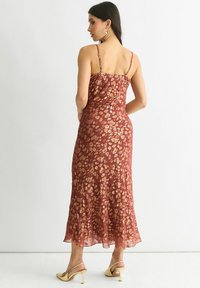 Satin midi dress in rust with a gold leopard print, strappy back, and flared hem. Paired with gold slingback heels.