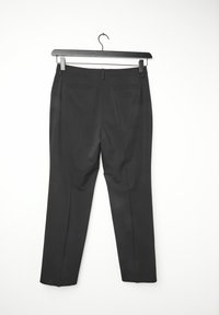 Pantalon noir sur mesure accroché à un cintre noir. Comprend deux poches arrière, des jambes droites et une finition soignée.