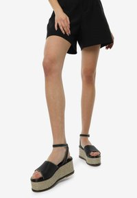 Sandalias de plataforma negras con suela de estilo yute trenzada, punta abierta y correas en el tobillo ajustables. Textura suave con acentos de costuras en contraste.