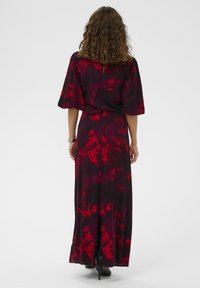 Maxi šaty z tmavé látky s červeným květinovým vzorem, krátkými rukávy, detailem klíčové dírky na zadní straně a rozparkem na boku pro lepší pohyb.