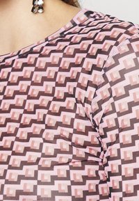 Tejido transparente y estampado con formas geométricas en rosa y marrón, con una textura suave y un ajuste relajado.