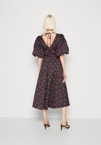 Vestido negro con estampado floral rosa, mangas abullonadas y escote profundo en V en la espalda, atado al cuello, con una silueta de longitud media y tela suave.