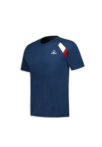 Camiseta de algodón azul marino de manga corta, con cuello redondo y detalle de rayas diagonales en blanco y rojo en el hombro izquierdo. Incluye un logo.