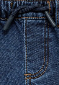 Detail z džínoviny s tmavě modrou barvou, kontrastním oranžovým prošíváním a černou šňůrkou pro nastavení v pase.