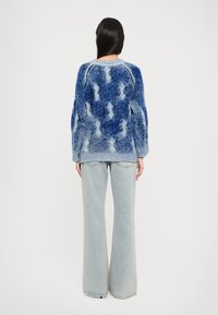Pulover tricotat în degrade de albastru, cu textură pufoasă și model abstract, combinat cu blugi evazați, decolorati.