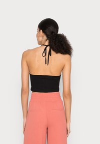 Top halter preto cropped com design de laço traseiro, combinado com calças largas rosa claro com cintura elástica e bolsos laterais.