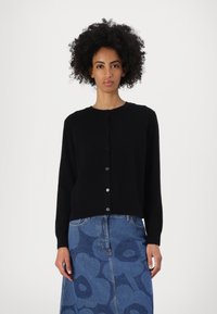 Svart cardigan med lange ermer, rund hals og frontknapping, laget av mykt stoff, kombinert med et mønstret blått denimskjørt.