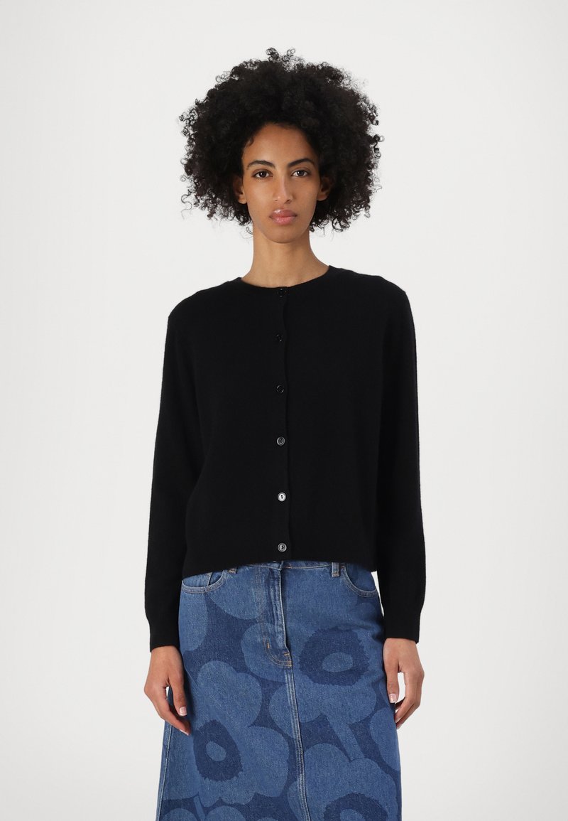 Svart cardigan med lange ermer, rund hals og frontknapping, laget av mykt stoff, kombinert med et mønstret blått denimskjørt.