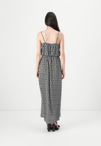 Abito maxi a motivi bianco e nero con spalline sottili, cintura elastica, silhouette fluida e tessuto testurizzato. Indossato con sandali con tacco a blocco.