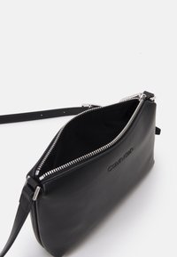 Borsa a mano in pelle nera con zip e tracolla in argento, caratterizzata da una superficie testurizzata e logo del brand visibile lungo il lato.