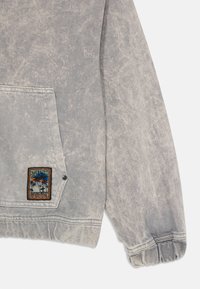 Sweatshirt en denim gris avec une finition texturée, doté d'une poche kangourou, de poignets élastiques et d'un patch coloré "Stay Fresh" cousu.