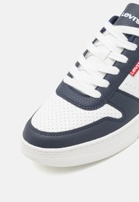 Granatowe i białe niskie trampki z teksturowaną skórzaną cholewką, perforowanym noskiem, białymi sznurowadłami oraz czerwonym logo Levi's z boku.