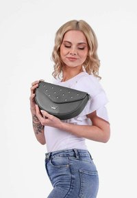 Šedá kožená kabelka s kulatým tvarem, s tečkovaným vzorem na přední strani a zipovým uzávěrem. Obsahuje kovové akcenty s logem.