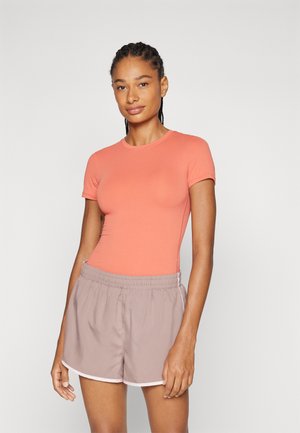 Top de manga corta color coral combinado con pantalones cortos marrón claro con ribetes blancos y una cinturilla elástica, creando un ajuste relajado.