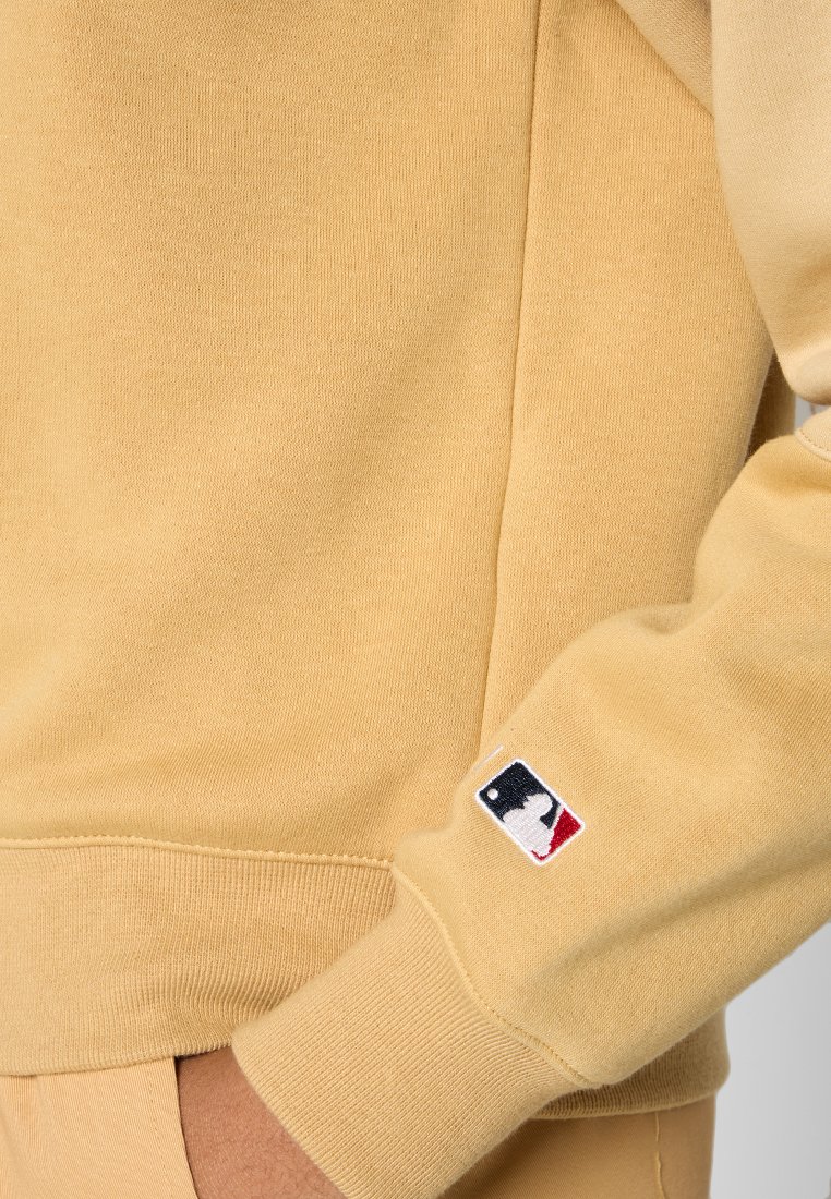 Żółta bluza crewneck z prążkowanymi mankietami, z małą naszywką logo MLB na lewym mankiecie. Miękka tekstura i casualowy styl.