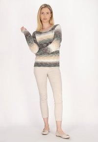 Pulover supradimensionat din tricot cu dungi orizontale în nuanțe de gri, bej și crem. Asortat cu pantaloni ajustați de culoare deschisă și pantofi plata.