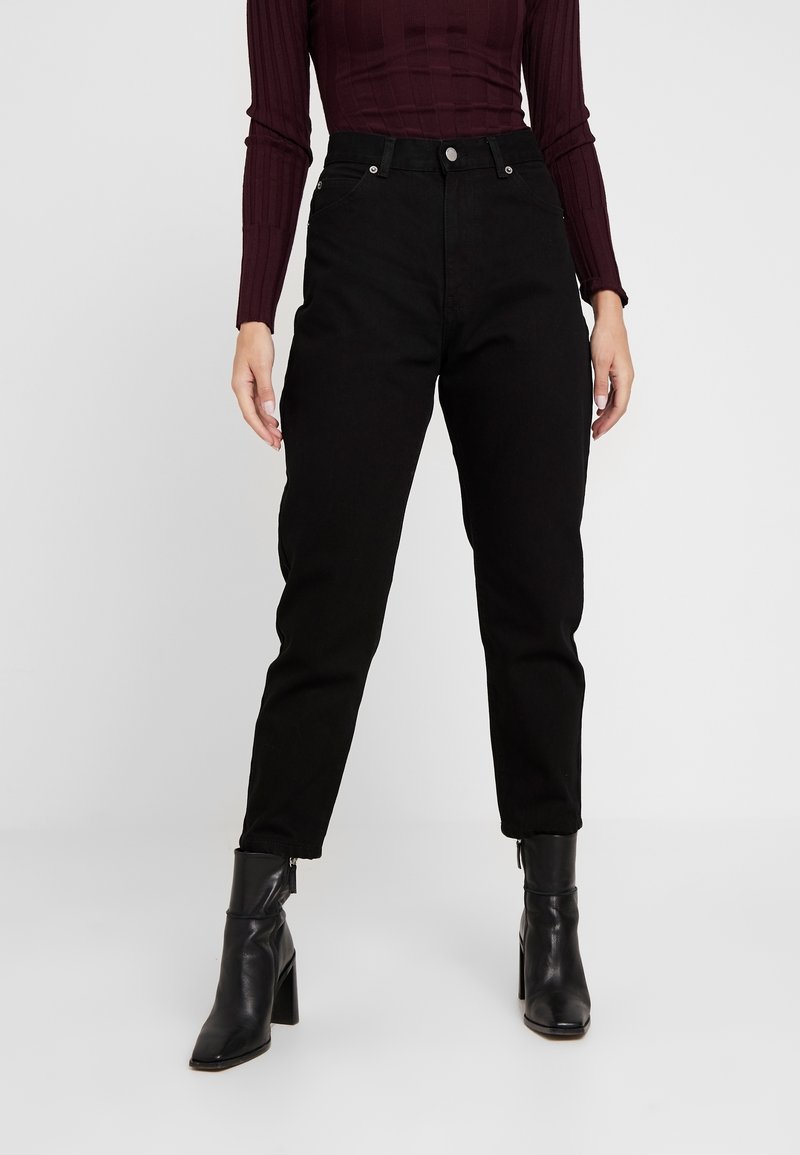 Svarta högmidjade jeans med rak bendesign, tillverkade av denim, ihopparade med svarta klackstövlar som går upp till ankeln och en ribbad bordeauxfärgad topp.