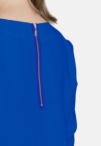 Blusa blu con zip nascosta sul retro. Tessuto liscio con una silhouette elegante e linee pulite.