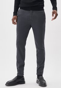 Szürke, letisztult anyagú, slim fit szabású nadrág, felhajtott szárakkal. Fekete mokaszinokkal viselve, kiegészítve az összes megjelenést.
