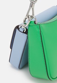 Borse in pelle verde e blu collegate tra loro da ganci e anelli in metallo argentato su uno sfondo bianco.
