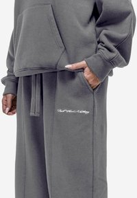 Grijze, cropped sweatshirt met een voorzak en een losse pasvorm, gecombineerd met bijpassende joggingsbroek met zijzakken en witte geborduurde tekst.