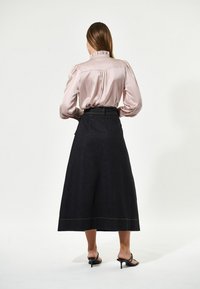 Gonna lunga in denim nera con vita alta e passanti per cintura, abbinata a una blusa in satin rosa chiaro con colletto arricciato e maniche a sbuffo.