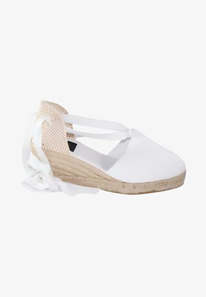 Cuña de esparto blanca con puntera cerrada, correa de tobillo en piel de serpiente beige y lazos blancos en el talón.