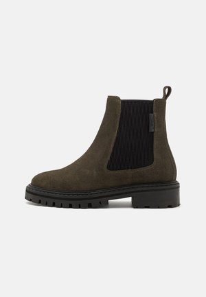 Botines de ante en verde oliva con paneles laterales elásticos negros, suela de goma texturizada y una lengüeta para facilitar el calzado.