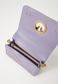 Bolsa de pele roxa com um fecho circular dourado, um bolso interno com zipper e um padrão texturizado em chevron no exterior.