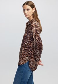 Leopardprint blouse van zachte, lichte stof met een kraag, lange mouwen en een ronde zoom. Gecombineerd met blauwe denim jeans.