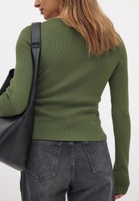 Ribbed green long-sleeve top with fitted design, paired with high-waisted dark gray jeans and a black tote bag. Smooth texture.