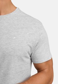 Graues Rundhalsausschnitt-T-Shirt aus weichem, strukturiertem Stoff. Mit einem kleinen weißen Logo auf der Brust und der Inschrift "EST. 1993".